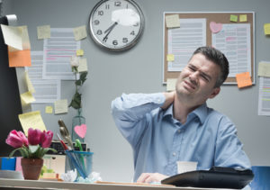 Tired businessman sitting at desk touching his painful neck.