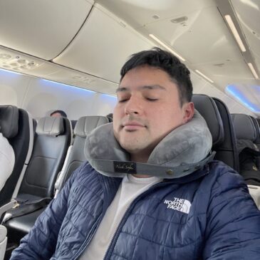 Traveler using Neck Sofa® pillow for neck support on airplane”