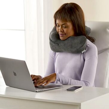 Woman using her grey Neck Sofa® Pillow while working on her computer at a white desk